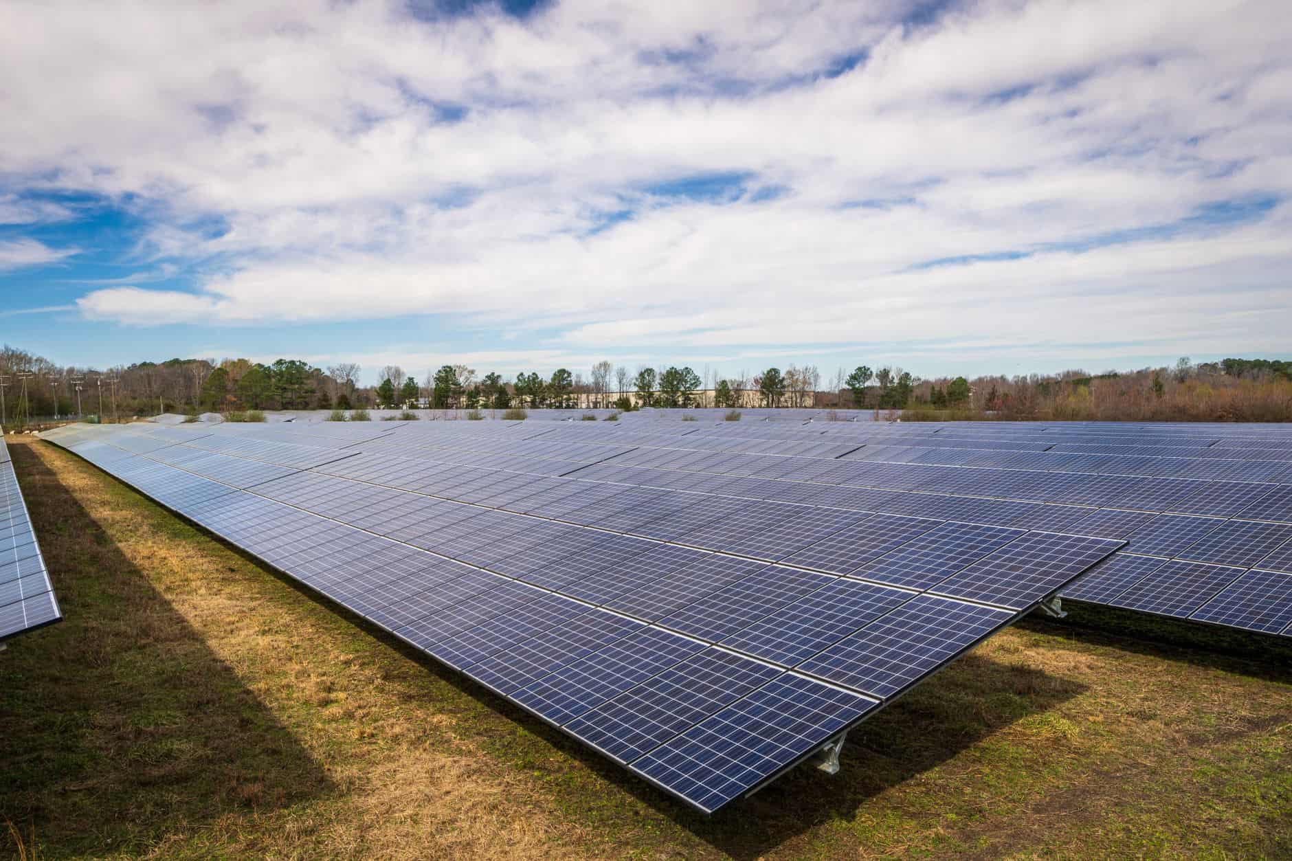 Large solar panel array in a field under a partly cloudy sky.
