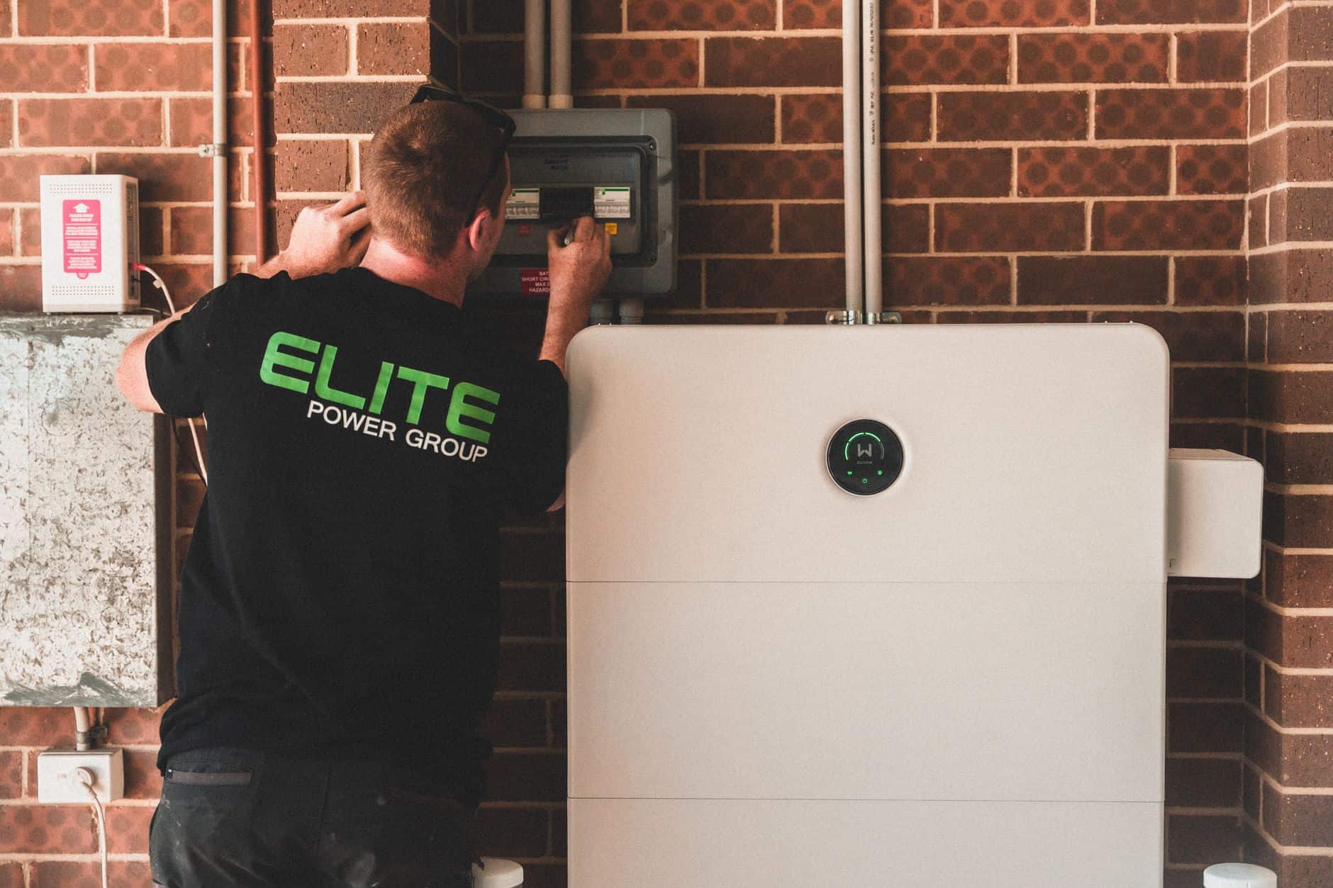 Technician inspecting solar power system control panel on brick wall.