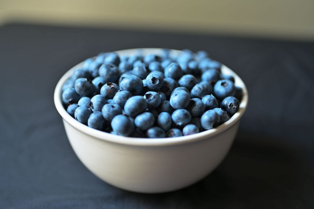A bowl filled with ripe, organic blueberries on a dark background.