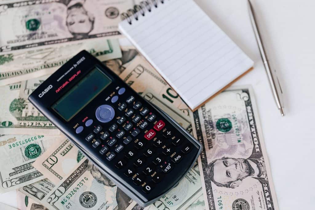 From above electronic calculator and notepad placed over United States dollar bills together with metallic pen for budge