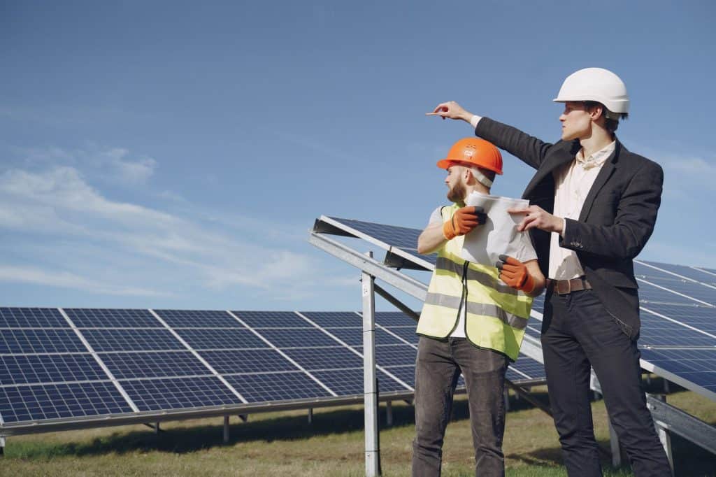Young businessman in formal outfit and foreman in yellow vest looking away while discussing working process against sola