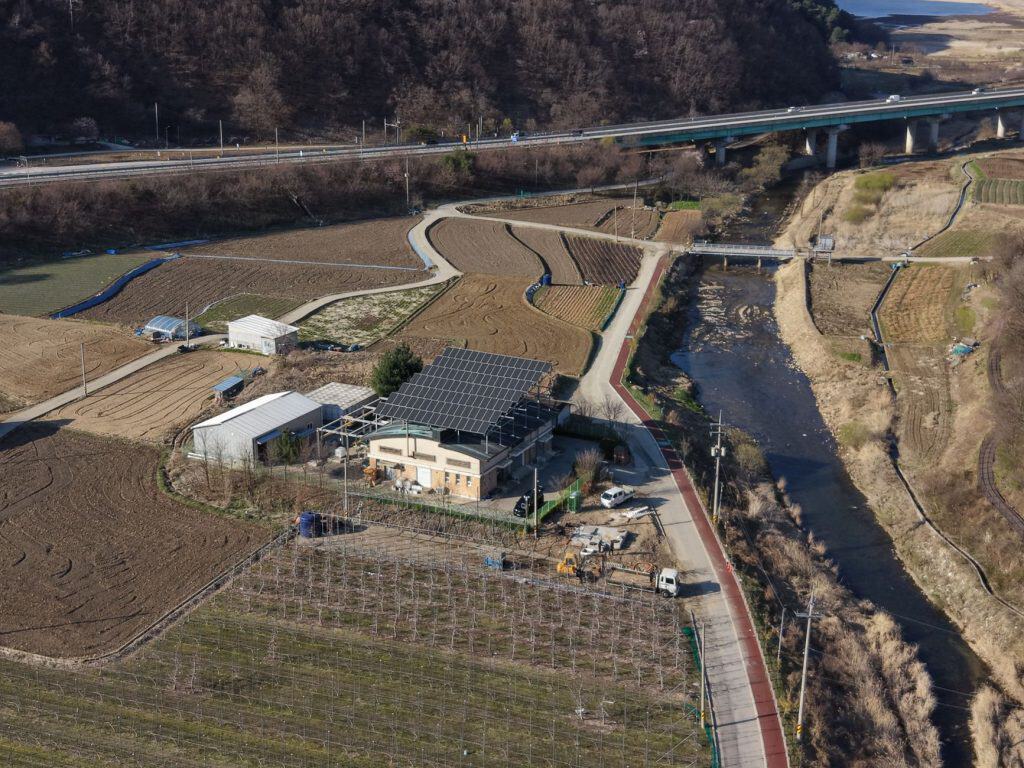 Aerial perspective of rural farmland featuring solar panels, fields, and a river.