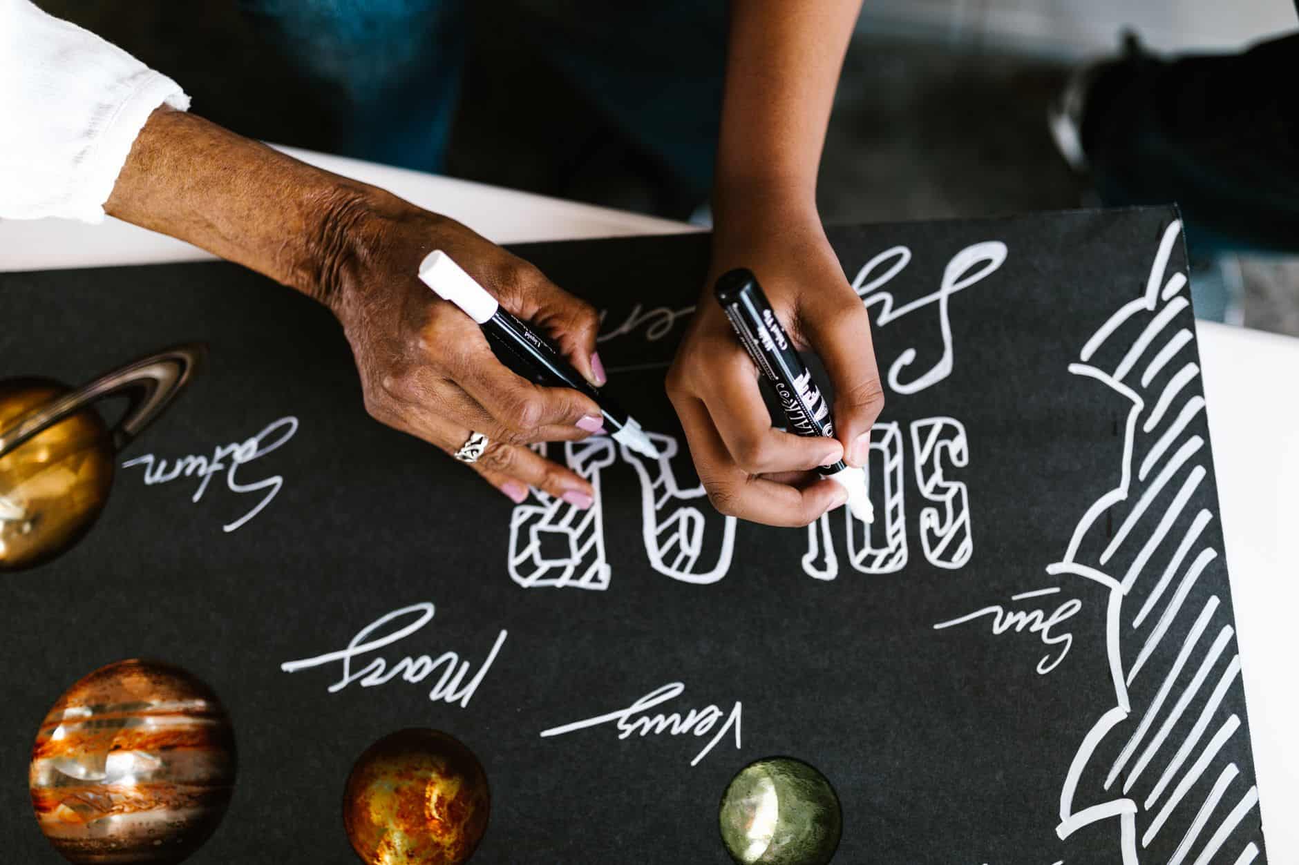 Hands writing on a space-themed poster with planets for a school project.